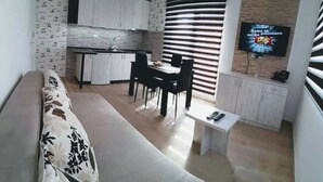 Un salon moderne comprenant un canapé, une table à manger avec des chaises, un coin cuisine avec des placards et un téléviseur fixé au mur.