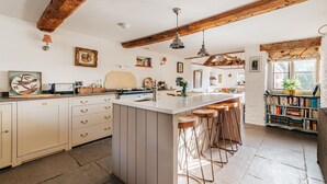 Una cocina con una isla central, taburetes de bar, una estantería y vigas de madera a la vista.