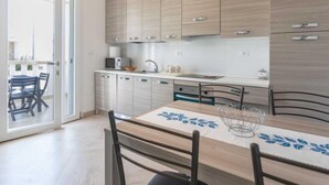 A modern kitchen with light wood cabinets, a stainless steel sink, and a dining table with chairs. - Gioia 1 by Interhome (Marina di Pescoluse)