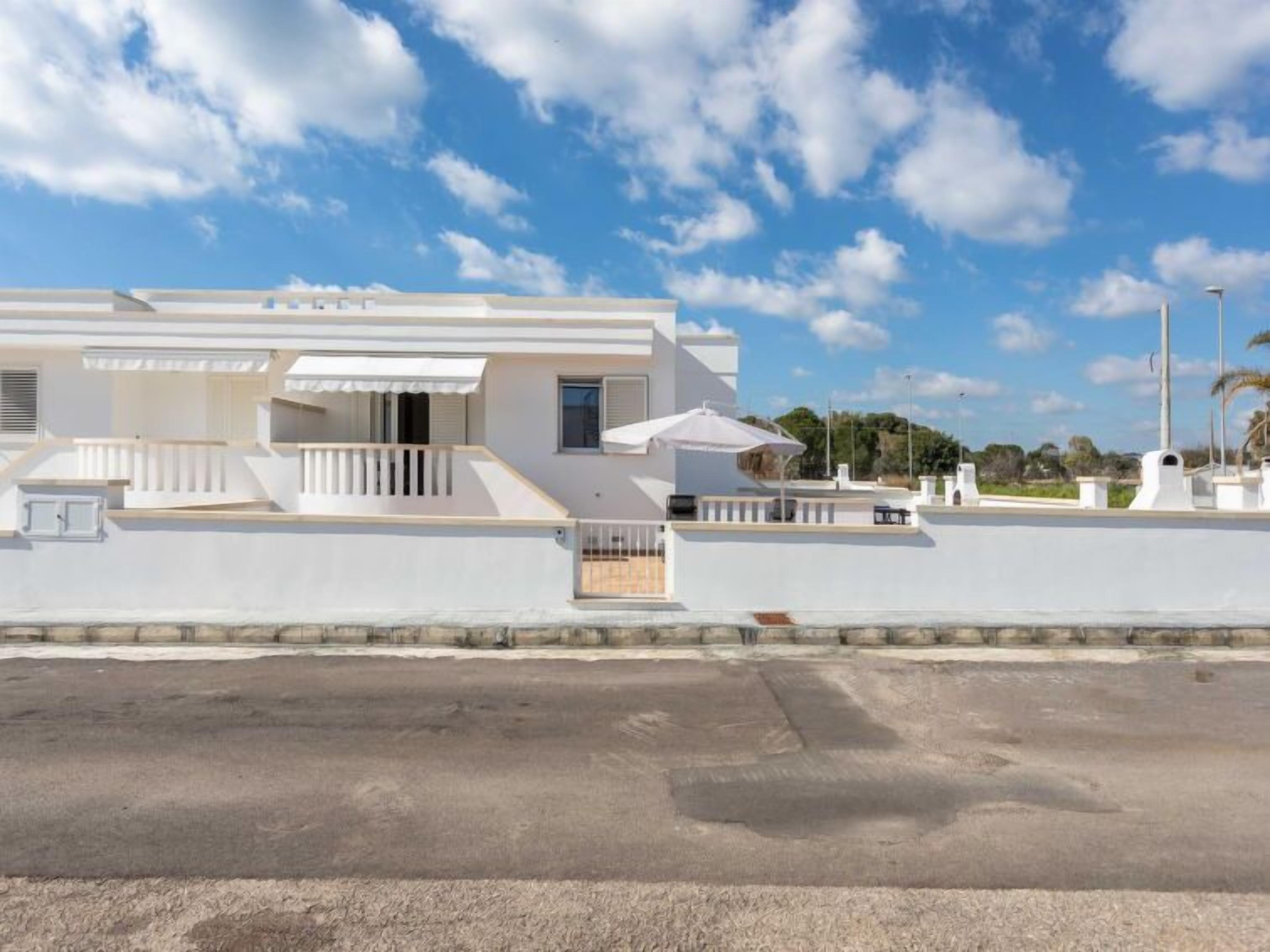 A modern white building with a flat roof, a balcony, and a covered outdoor seating area.