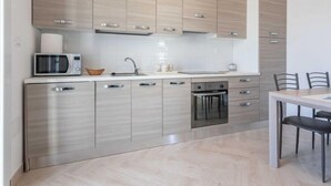 A modern kitchen with light wood cabinets, a microwave, a sink, and a dining area with a table and chairs. - Gioia 1 by Interhome (Marina di Pescoluse)