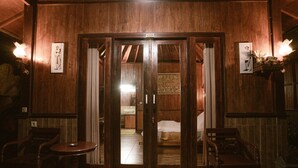 Un interior de madera con una puerta corredera que da a un dormitorio, dos sillas de madera y una pequeña mesa.