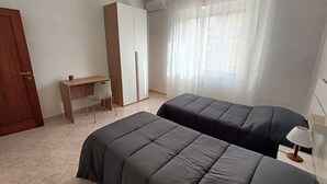 Een slaapkamer met twee bedden, een bureau en een garderobe.