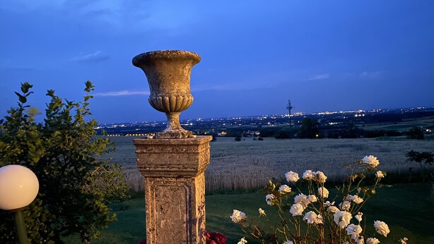 Een stenen pilaar met een decoratieve vaas, omringd door witte en rode bloemen, met uitzicht op een stad bij zonsondergang.
