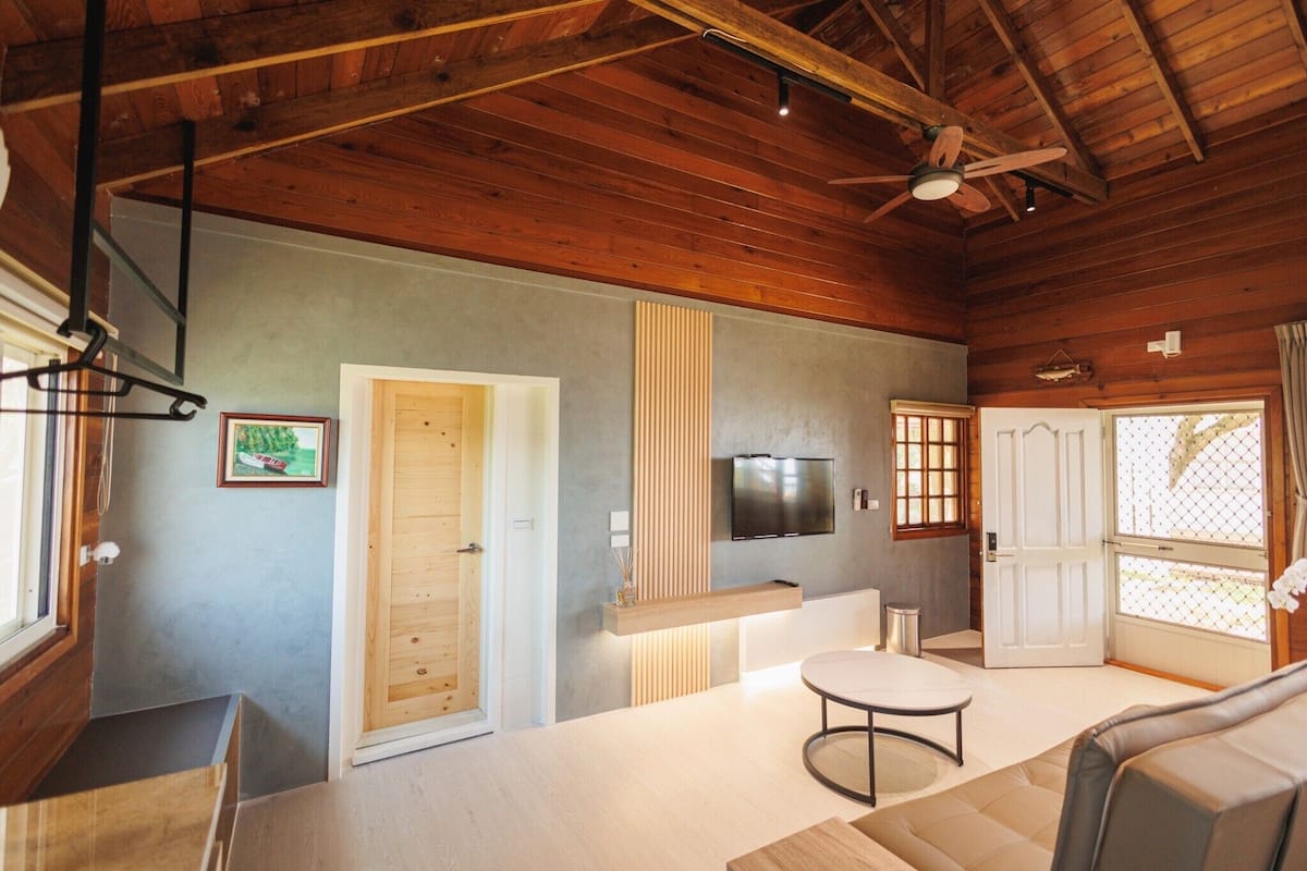 A modern interior with a wooden ceiling, a flat-screen TV mounted on the wall, a round table, and a sofa.