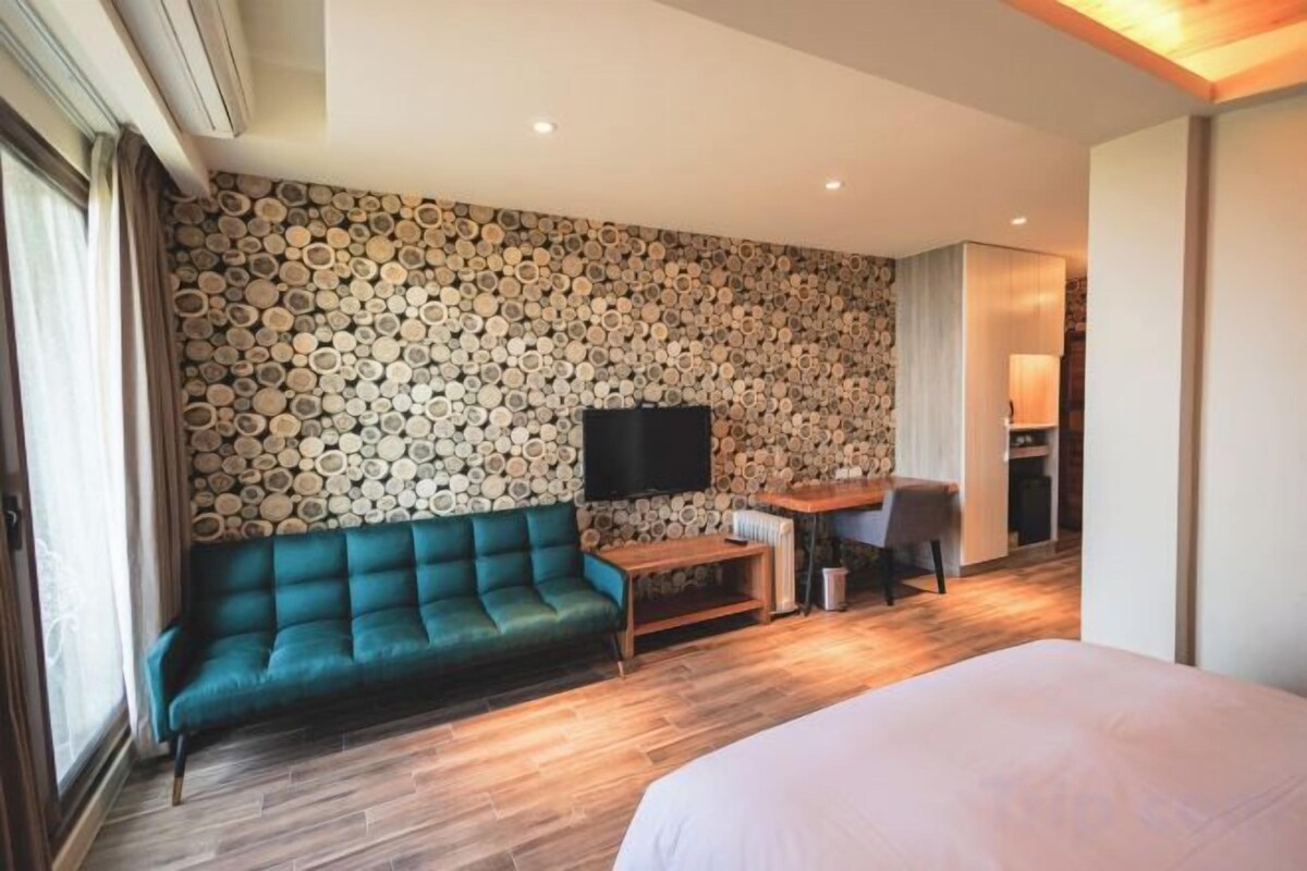 Ett hotellrum med en grön soffa, en platt-TV, ett skrivbord i trä och en säng.
