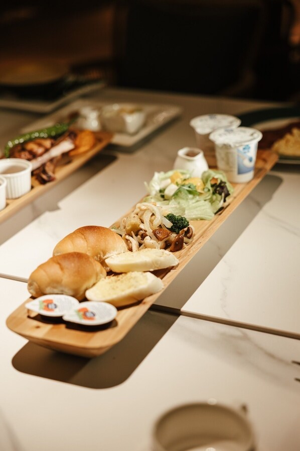 A long wooden serving tray with various food items, including a croissant, bread, and a salad. - Chill Hill Cottage (Taichung)