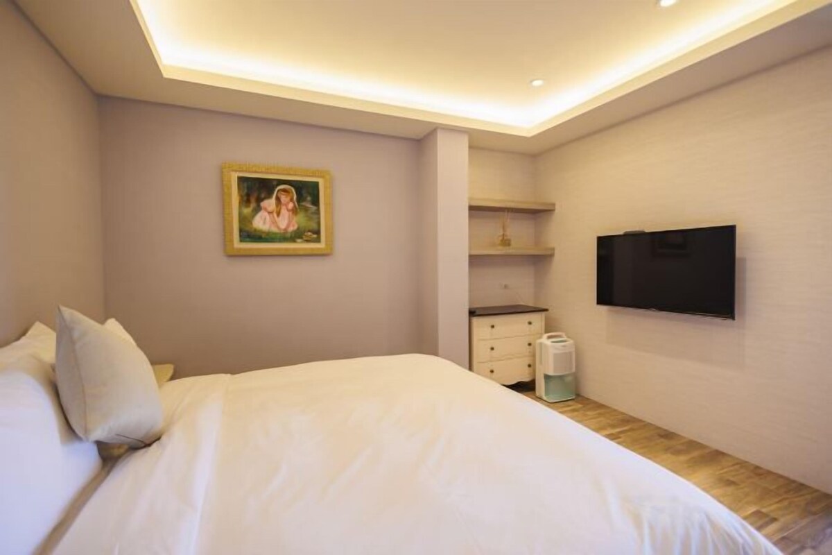 A bedroom with a bed, a television mounted on the wall, and a painting on the wall.