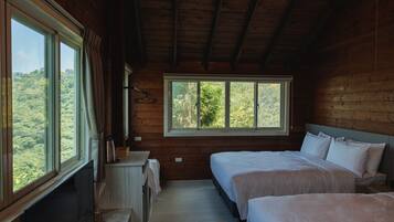 A cabin with two beds, a wooden interior, and a large window offering a forest view.