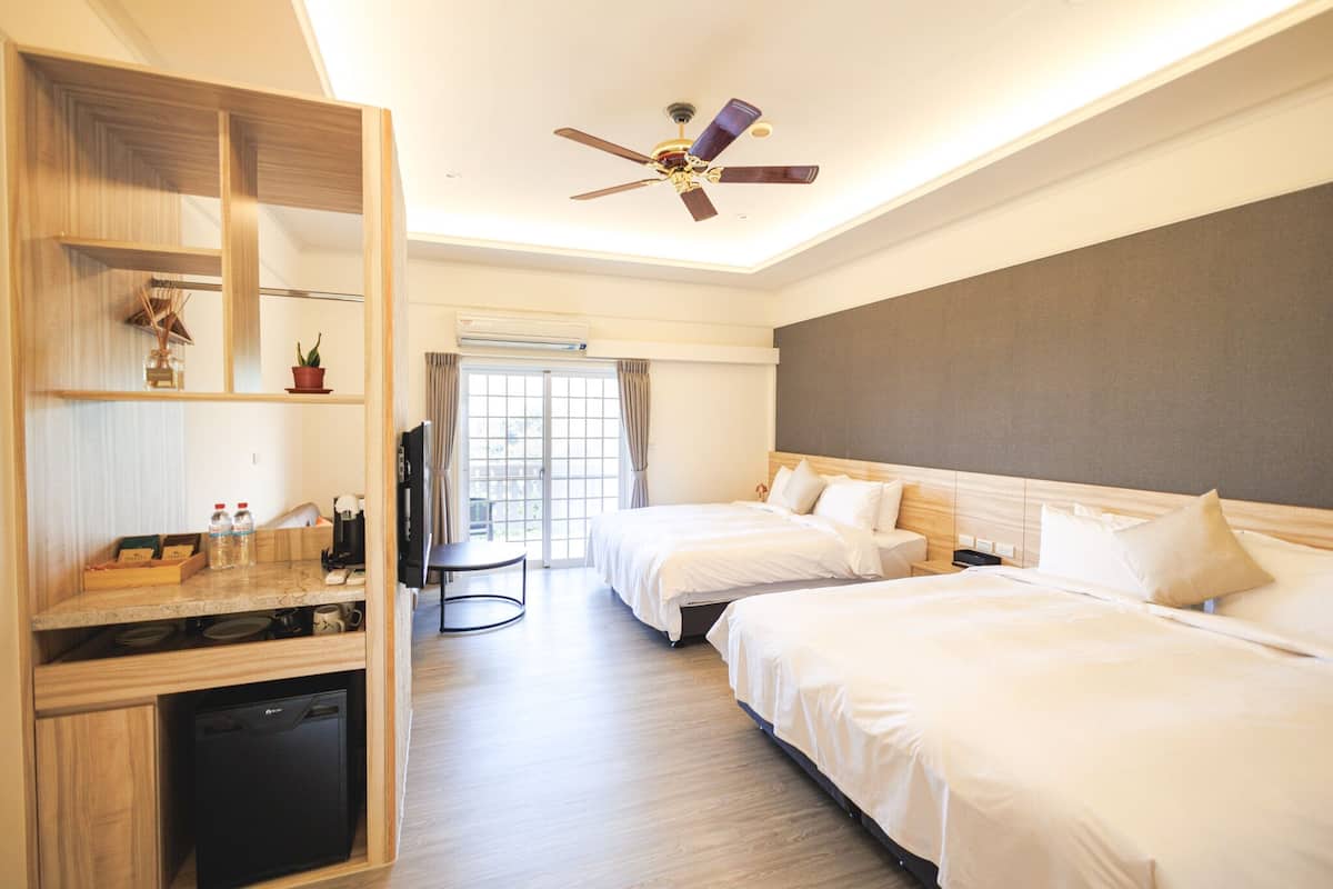 A hotel room with two beds, a desk with a dishwasher, a ceiling fan, and a window with curtains.