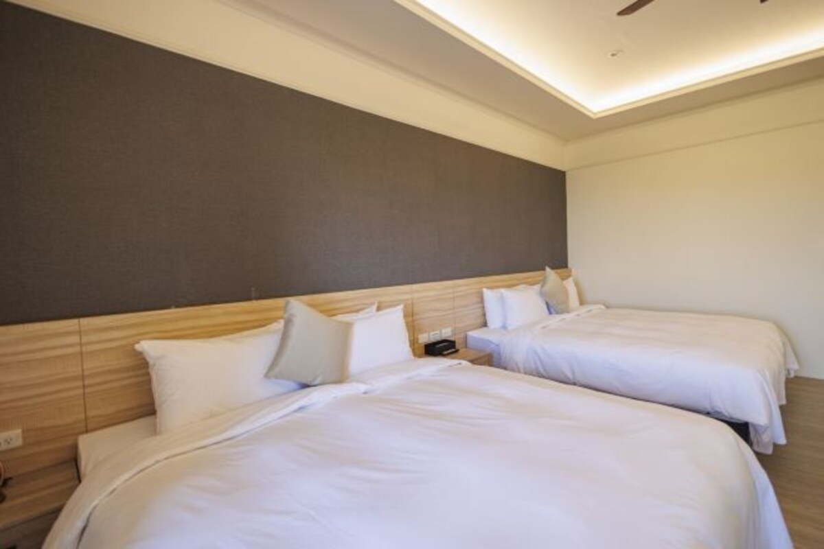 A hotel room with two single beds, a wooden headboard, a nightstand, and a ceiling fan.