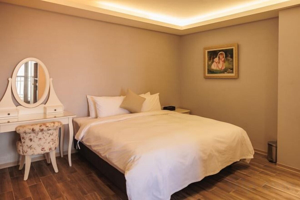 A bedroom with a bed, a nightstand, a dresser, a chair, and a painting on the wall.