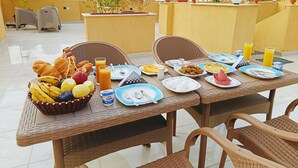 A rooftop dining area with wicker furniture, a variety of breakfast foods, and a cityscape view in the background. - DISCOVER Pyramids inn  (Giza)