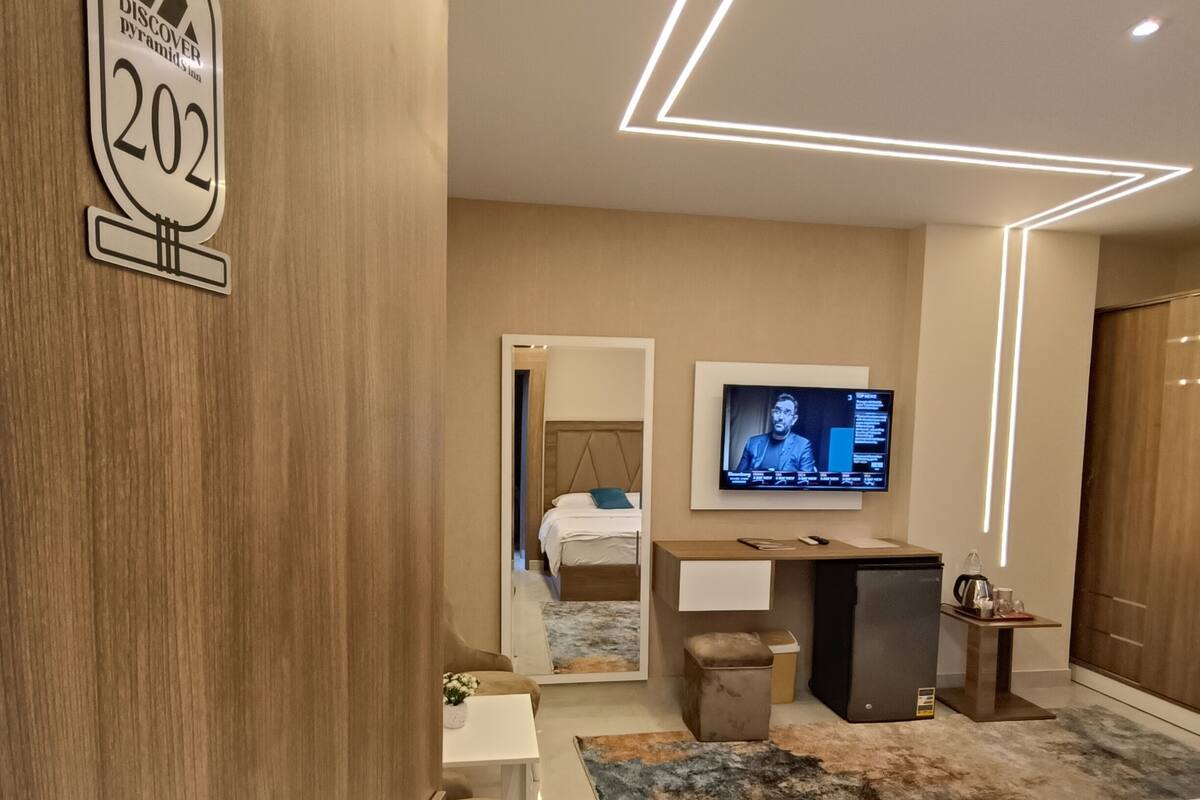 A modern hotel room with a bed, a desk, a television, and a mirror.