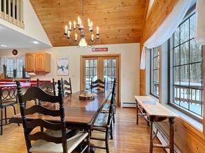 A wooden interior with a dining table, chairs, a chandelier, and large windows. - Beechwood Home - 4 Bedrooms and 3 Baths, sleeps 10 (Mendon)