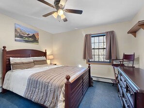 A bedroom with a bed, a desk, a chair, a ceiling fan, a window with curtains, and a painting on the wall. - Beechwood Home - 4 Bedrooms and 3 Baths, sleeps 10 (Mendon)