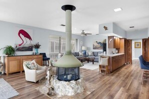 A living room with a stone fireplace, a sofa, a coffee table, and a dining area with wooden cabinets. - Colonel's Cottage- Sanibel Beach Retreat, Fantastic Amenities (Sanibel)