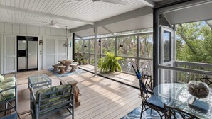 Un espace extérieur abrité, doté d’un ventilateur de plafond, d’un plancher en bois et d’une table en verre avec des chaises.
