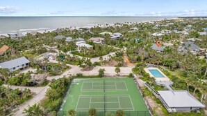 Vue aérienne d’un quartier résidentiel avec un court de tennis, une piscine et des maisons entourées de verdure.