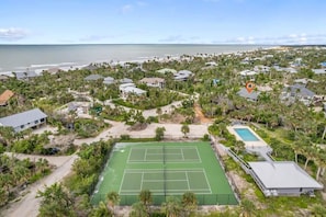 Vista aérea de una zona residencial con cancha de tenis, piscina y casas rodeadas de vegetación.