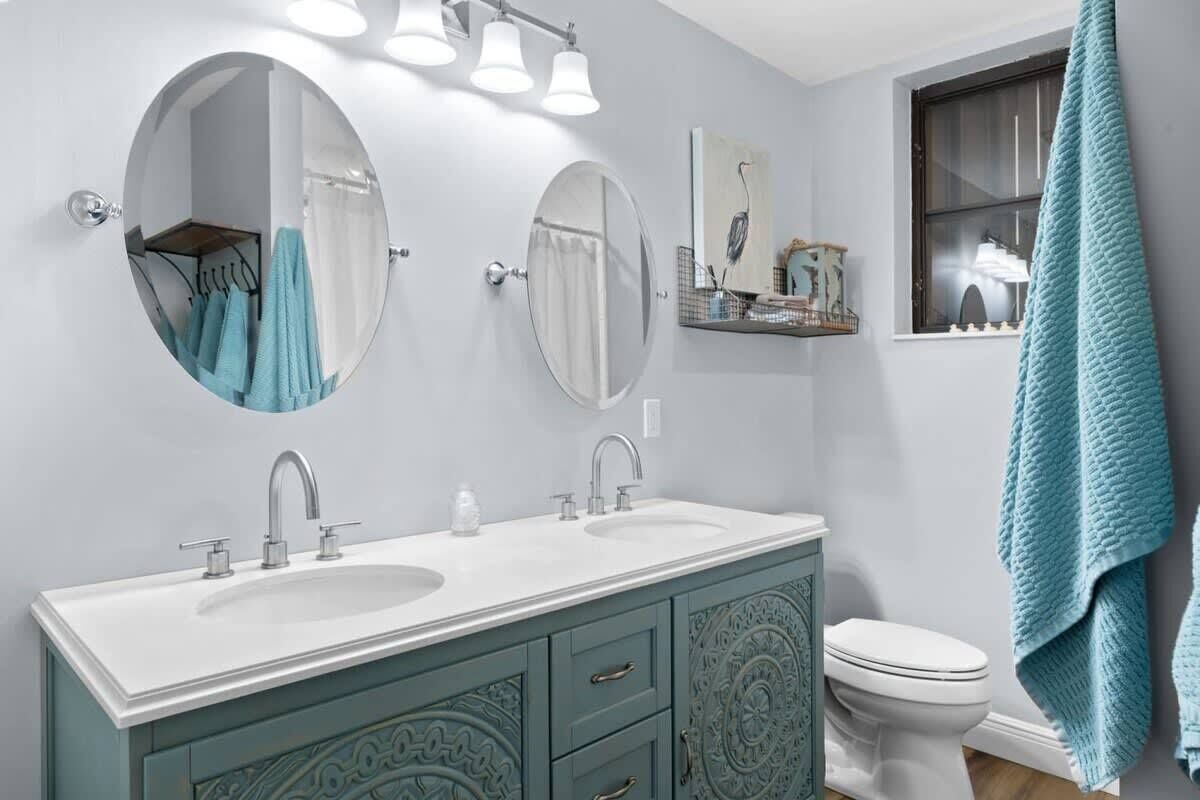 Une salle de bain avec deux lavabos, des toilettes et une fenêtre sur laquelle est accrochée une serviette.