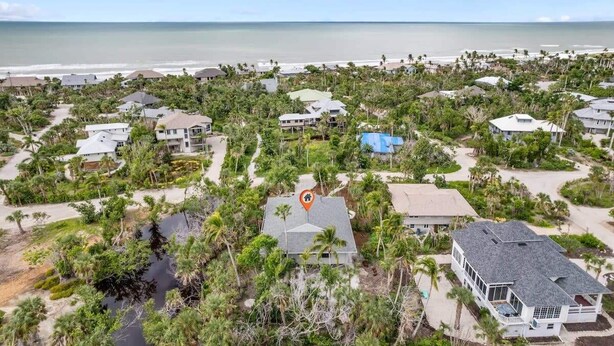 Un quartier résidentiel situé sur la côte, avec des maisons entourées de verdure et une plage en arrière-plan.