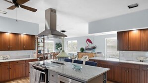 Une cuisine moderne avec des meubles en bois, un îlot central, des appareils électroménagers en acier inoxydable et un ventilateur de plafond.