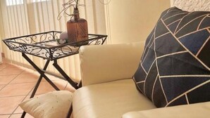 Ein Wohnzimmer mit einem beigefarbenen Sofa, einem gemusterten Kissen, einem kleinen Tisch mit einer Vase und einem Sessel.