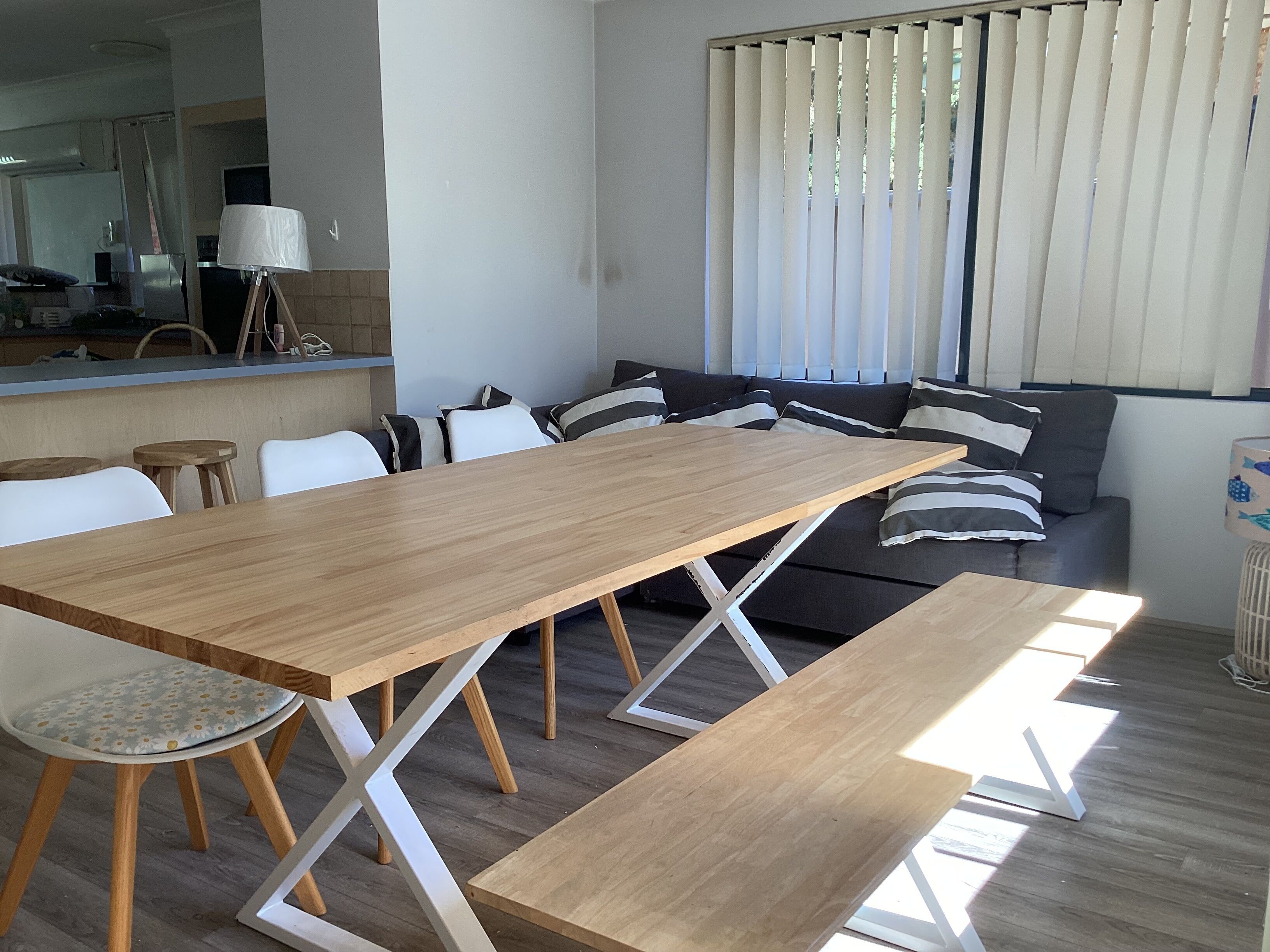 A modern living room with a wooden dining table, white chairs, and a black sofa with striped cushions.