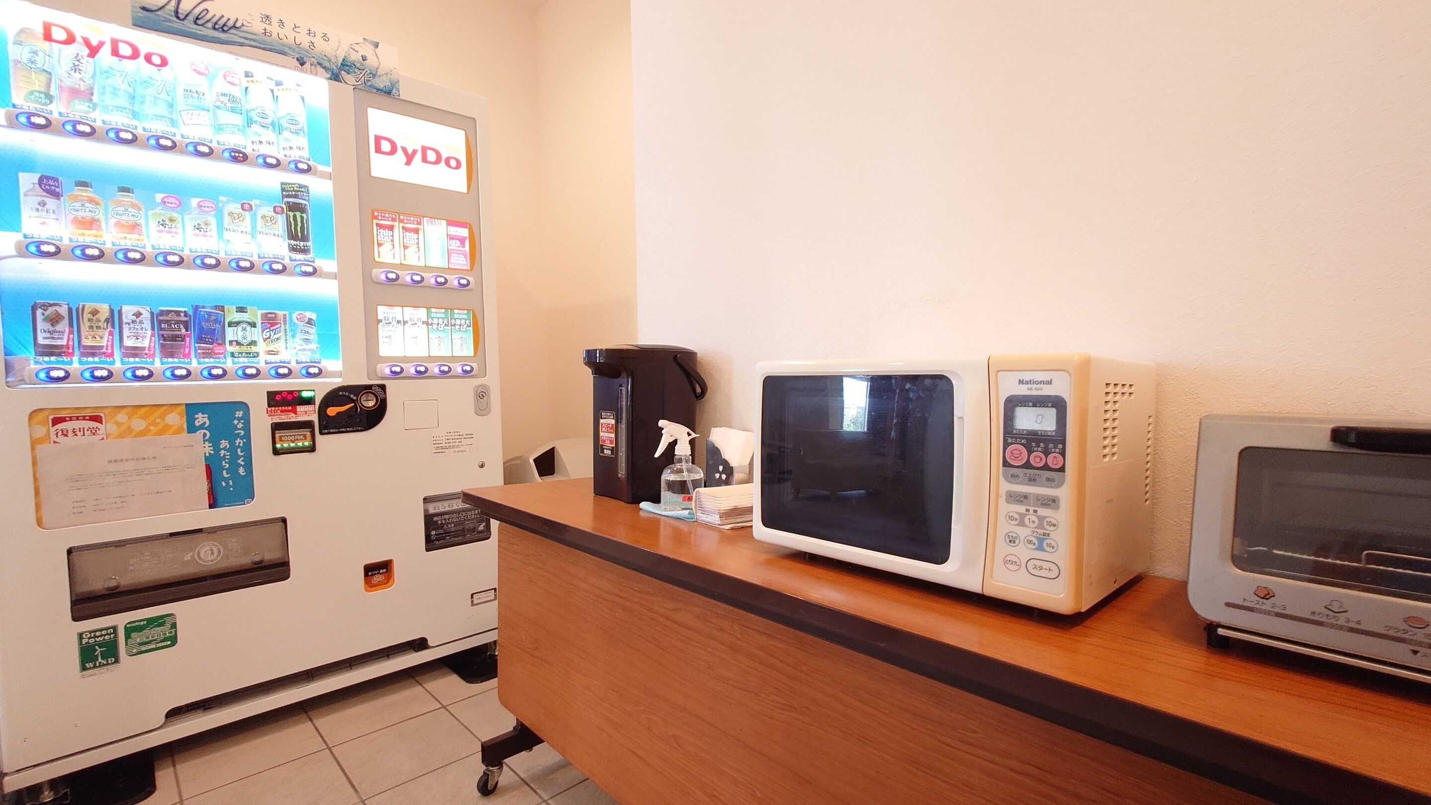 Un distributeur automatique proposant diverses boissons et collations, un four à micro-ondes et une machine à café, le tout installé sur un comptoir.