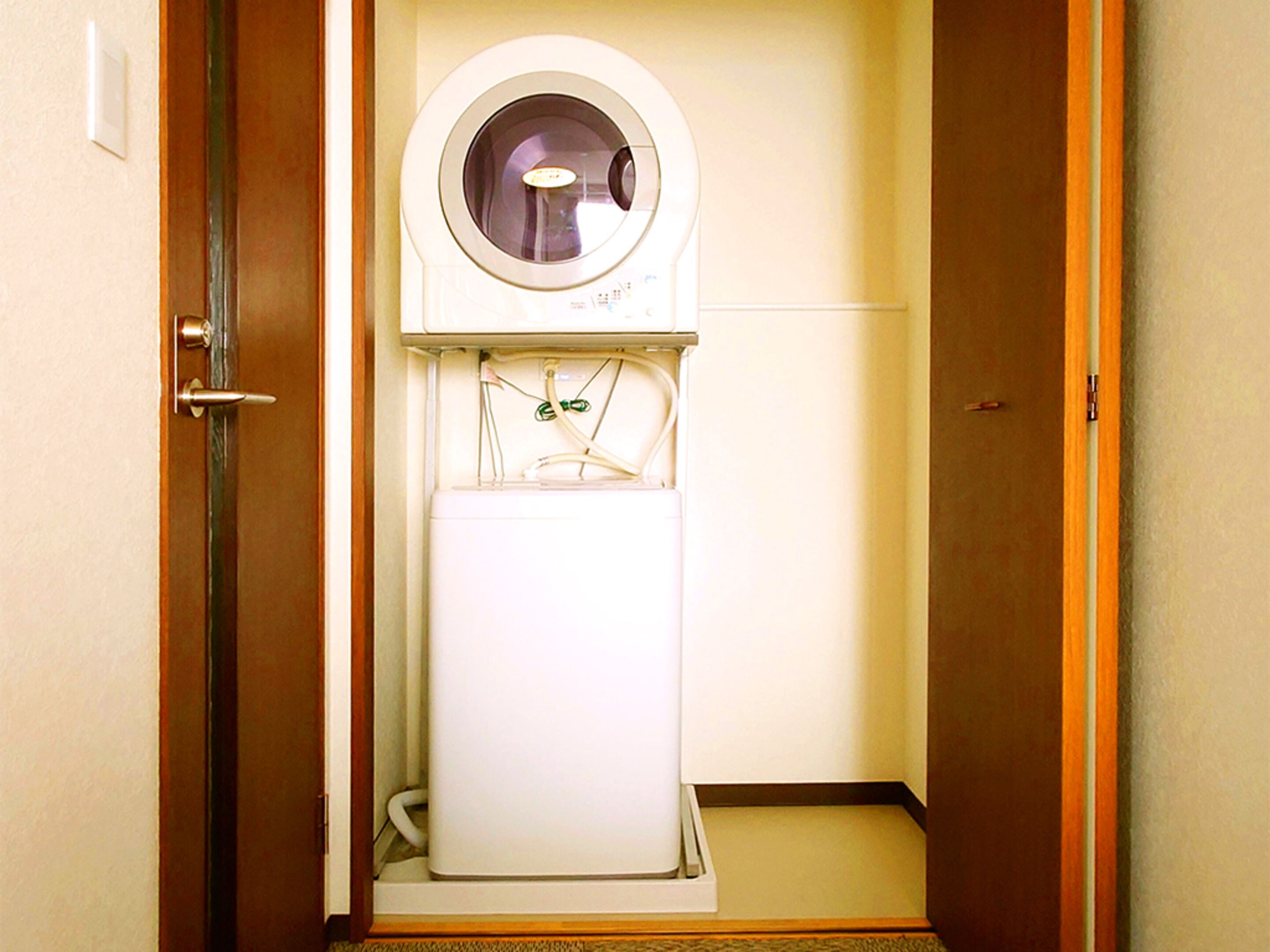 A compact, white, wall-mounted water dispenser in a narrow hallway with wooden doors and a carpeted floor.