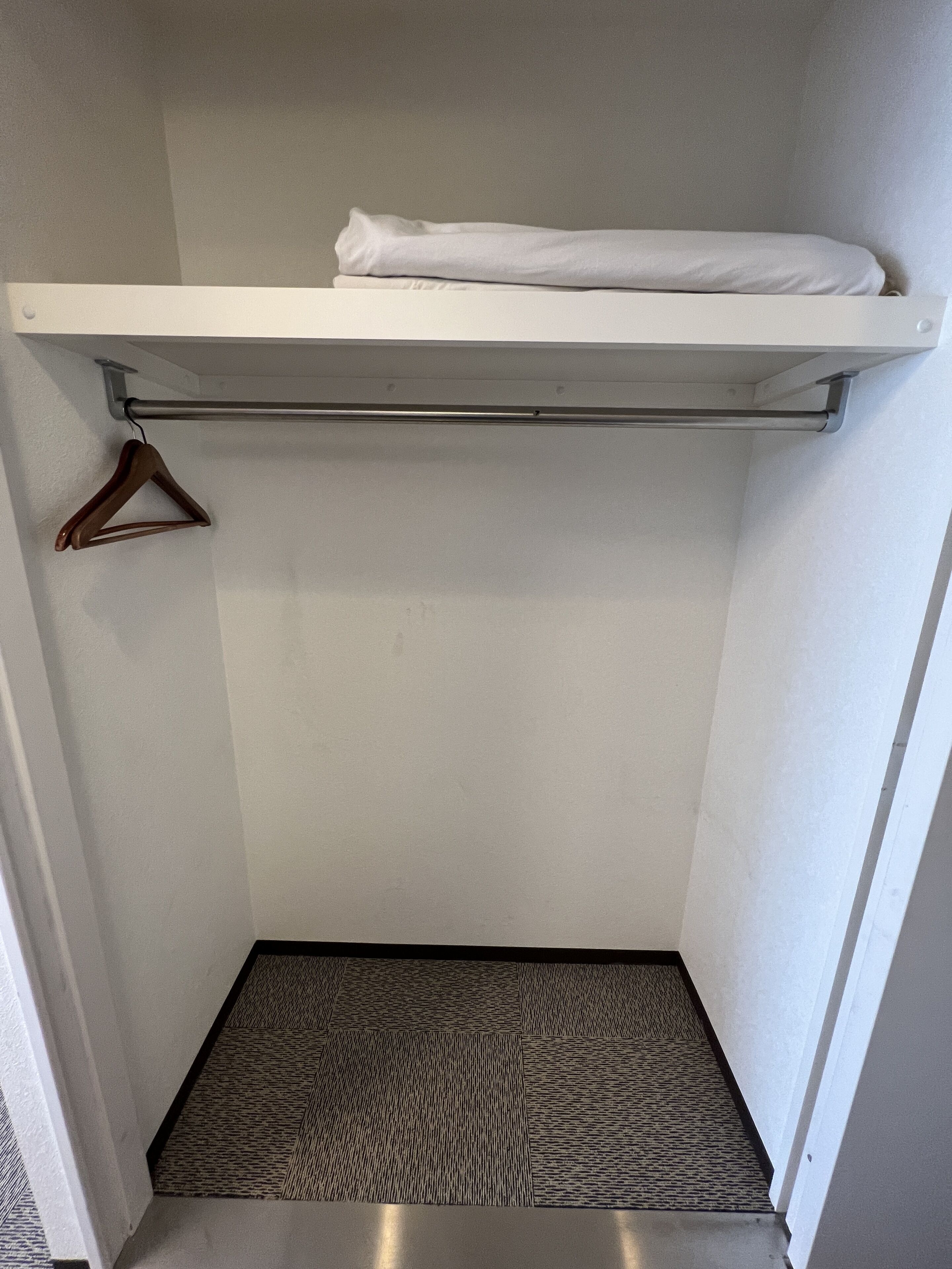 A small walk-in closet with a hanging rod, a patterned rug, and a white shelf.