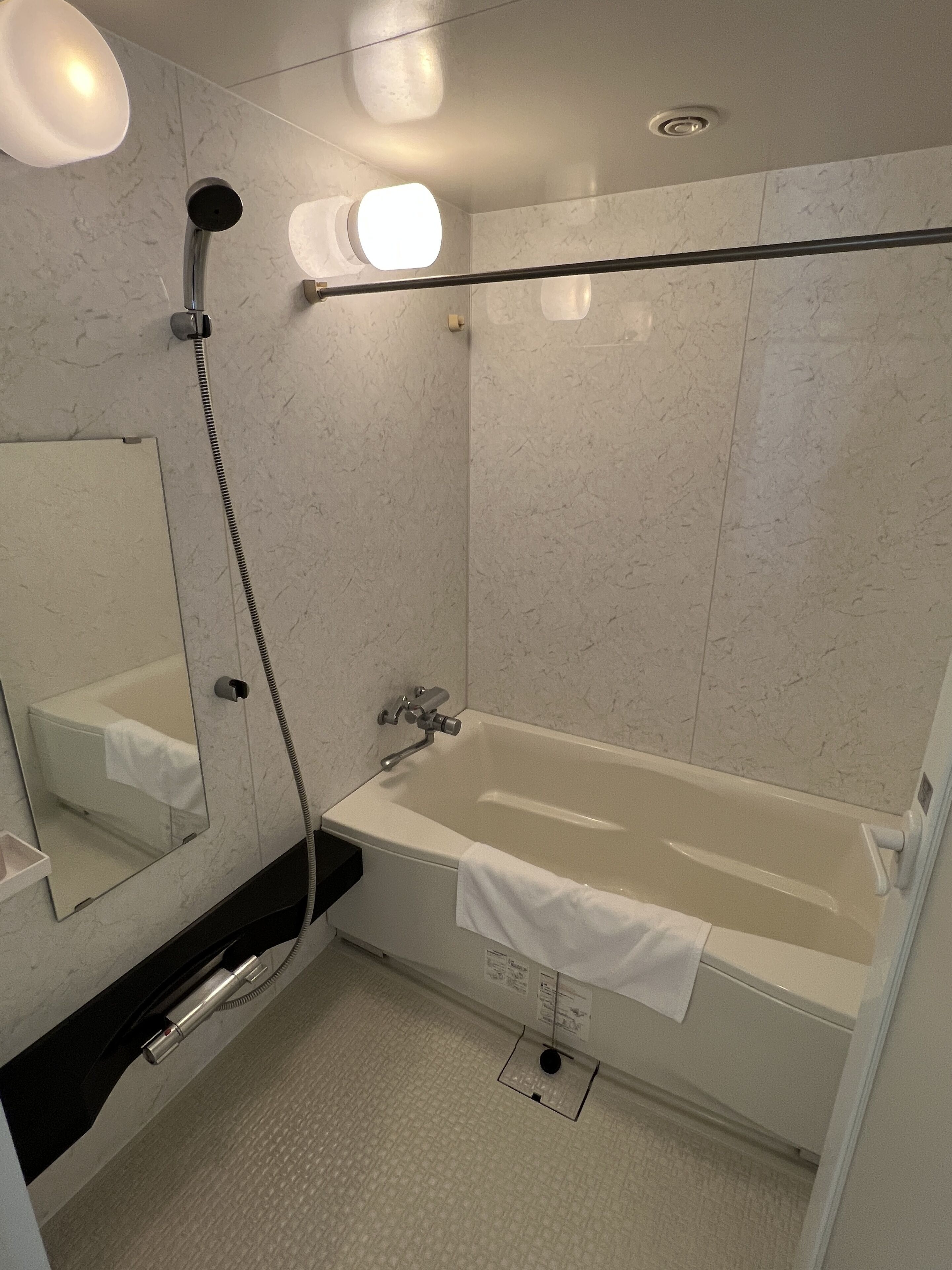 Un baño moderno con bañera, cabezal de ducha manual, toallero y espejo.