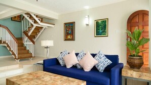 A living room with a blue sofa, wooden coffee table, and a staircase with wooden railings. - Captivating 2-Bed Town-House in Kingston (Kingston)