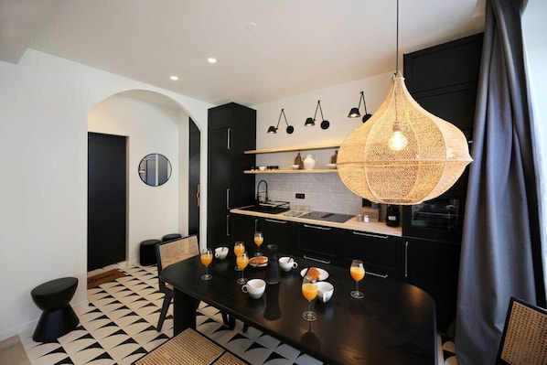 A modern kitchen with black cabinets, a black dining table, and a hanging light fixture.
