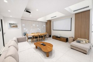 A modern living room with a dining area, a sofa, a coffee table, a TV, and a projector screen.