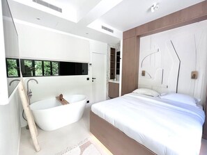 A modern bedroom with a large bed, a freestanding bathtub, and a built-in wardrobe.