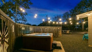 A hot tub in a backyard with string lights, a wooden fence, and a covered seating area. - 3 Bedroom Home / Hot Tub / Firepit / Game room (Fredericksburg)