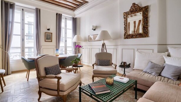 A well-lit living room with a wooden ceiling, a sofa, two armchairs, a coffee table, and a dining area with a chair and table.