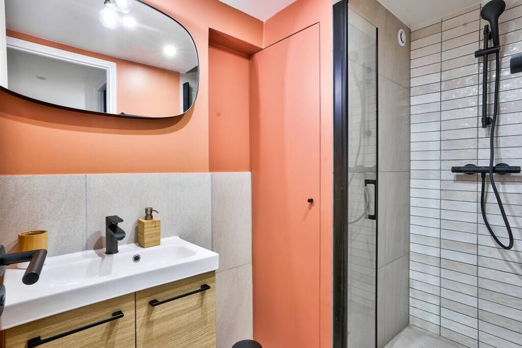 Une salle de bain avec un lavabo blanc, un miroir, un meuble en bois et une douche fermée par des parois de verre.