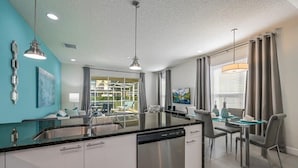 Eine moderne Küche mit Geschirrspüler, ein Essbereich mit Glastisch und Blick ins Freie.