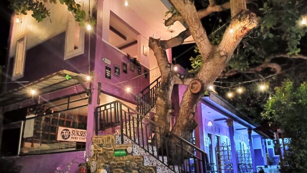 A building with a purple facade, a stone staircase, and a sign for 'Sukes Home Stay'. - Homestay Sukses Tambora (Pekat)