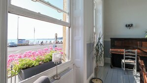 A room with a large window overlooking a street with cars and a cyclist. There is a radiator, a potted plant, and a wooden bench. - The Esplanade (Weymouth)