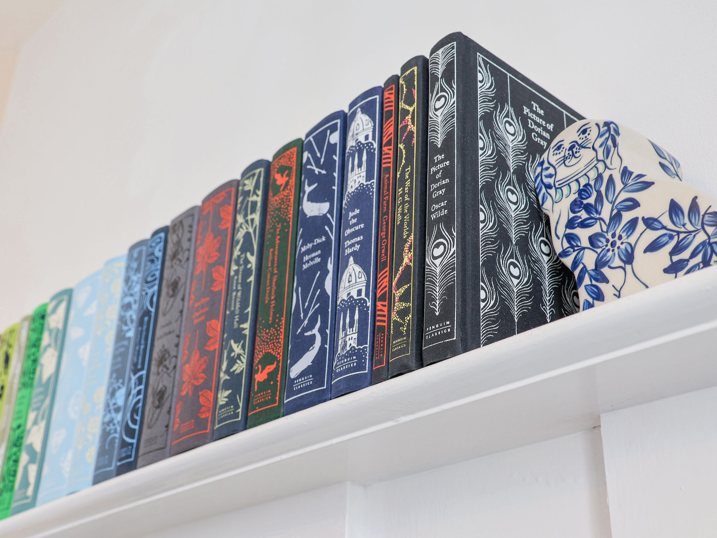 A row of books with various designs and titles on a white shelf.