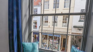 A window seat with cushions, overlooking a street with a bookshop and other buildings. - Book House (Whitby)