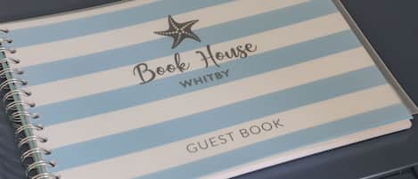A spiral-bound notebook with a blue and white striped cover, labeled "Book House WHITBY GUEST BOOK."