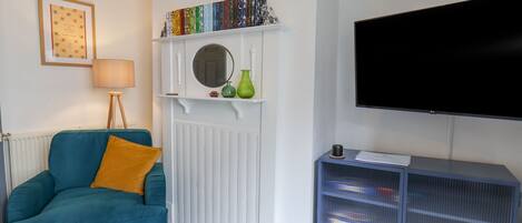 A living room with a teal sofa, a white fireplace, a bookshelf, and a TV.