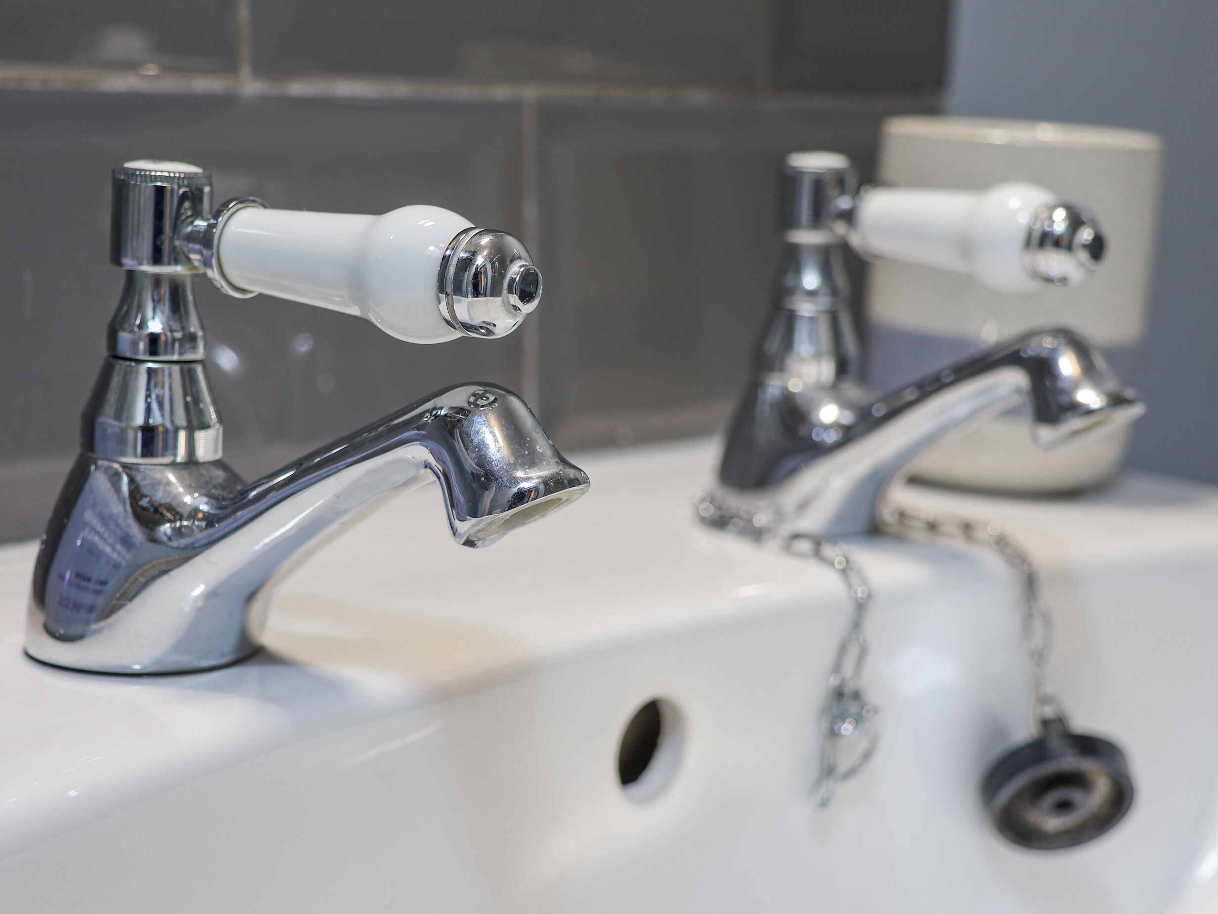 A bathroom sink with two chrome faucets, one with a white handle and the other with a silver handle.