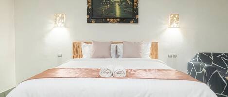 A neatly made bed with a white and pink bedspread, two wall-mounted lights, and a framed painting above the bed.