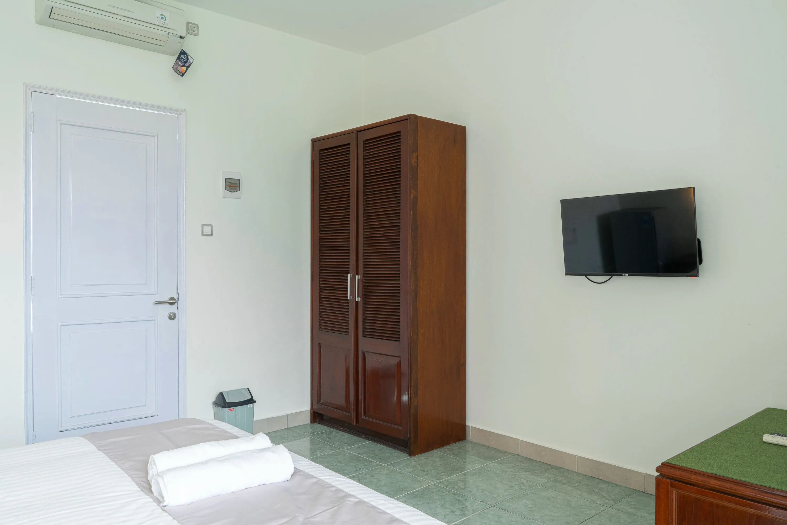 Une chambre à coucher avec un lit, une armoire, un téléviseur et une poubelle.